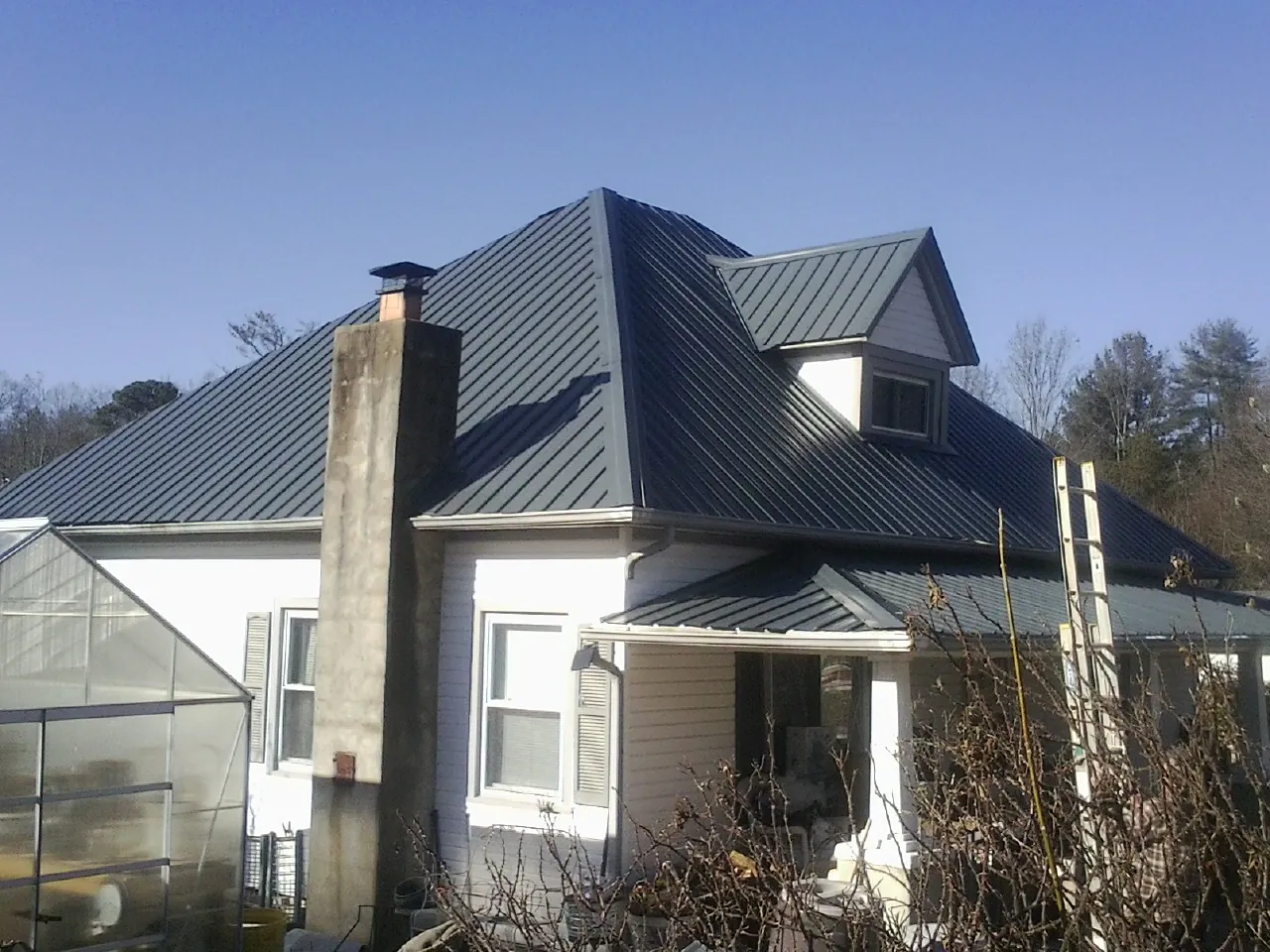Dark blue standing seam metal roof on a white farmhouse with dormer — Slate & Tile Roof Repair by Roofing Brothers in Shawsville