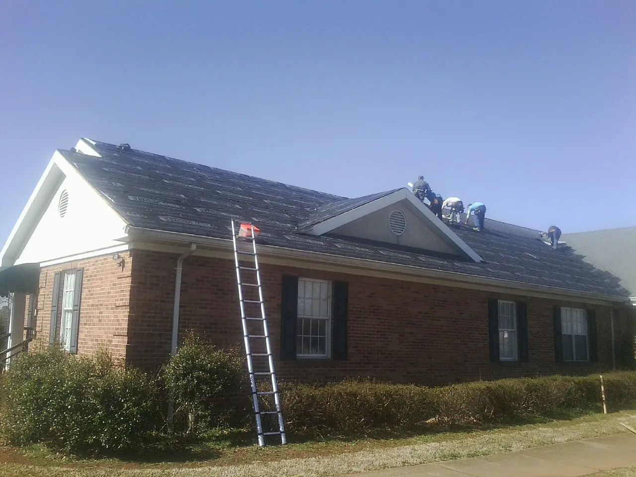 Crew tearing shingles off a brick ranch roof with a ladder set — Metal Roof Repair work by our crew in Shawsville