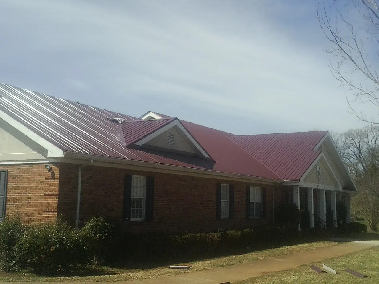 Red metal roof with gabled entries on a long brick building, from a Hail Damage Roof Repair job in Shawsville