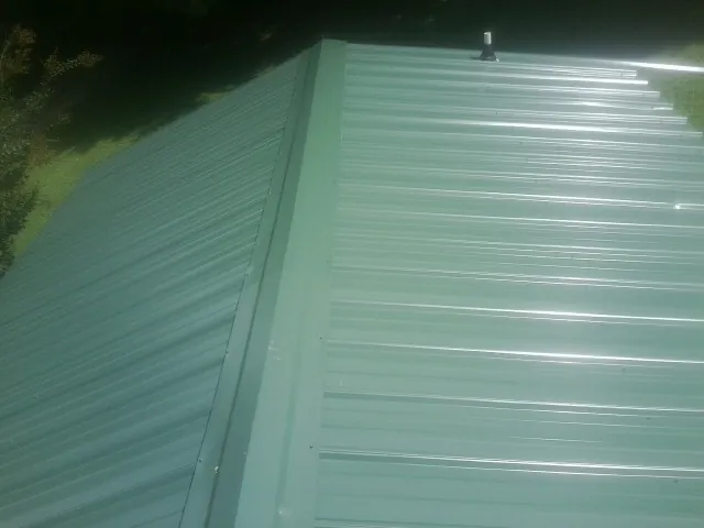 New green metal panels meeting at the ridge of a roof — Flat Roof Repair work by our crew in Shawsville