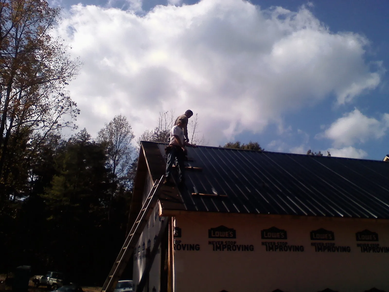 Roofer fastening dark metal panels high against a cloudy sky, from a Roof Inspection job in Shawsville