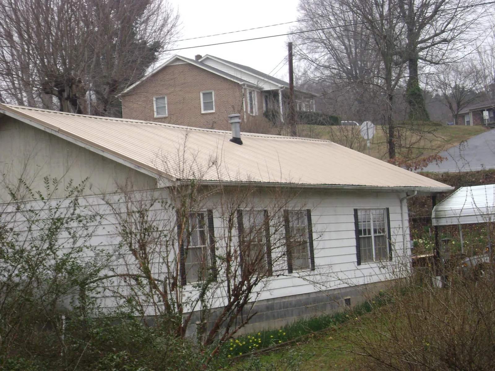 Tan metal roof on a white sided house set into a hillside — Commercial Roofing by Roofing Brothers in Shawsville
